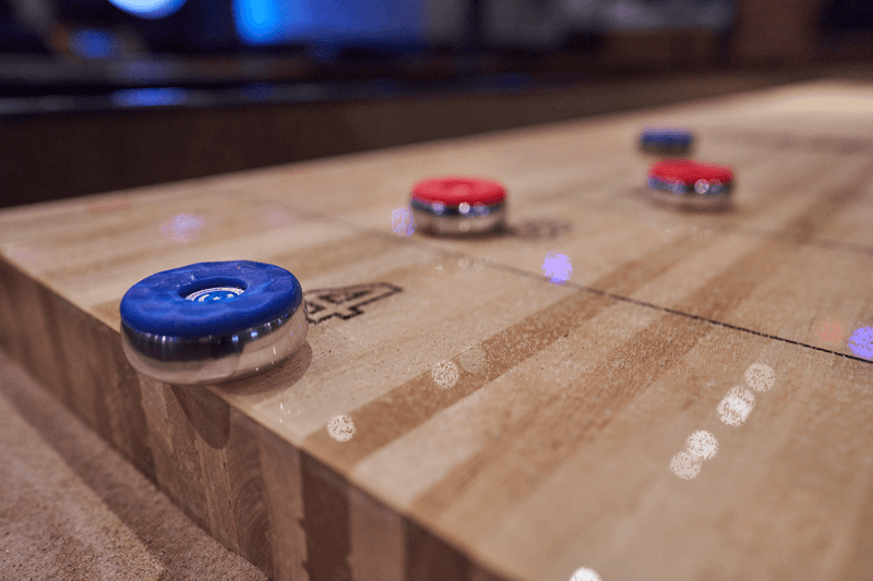 Shuffleboard, röda och blå puckar, en blå på kanten, fem poäng
